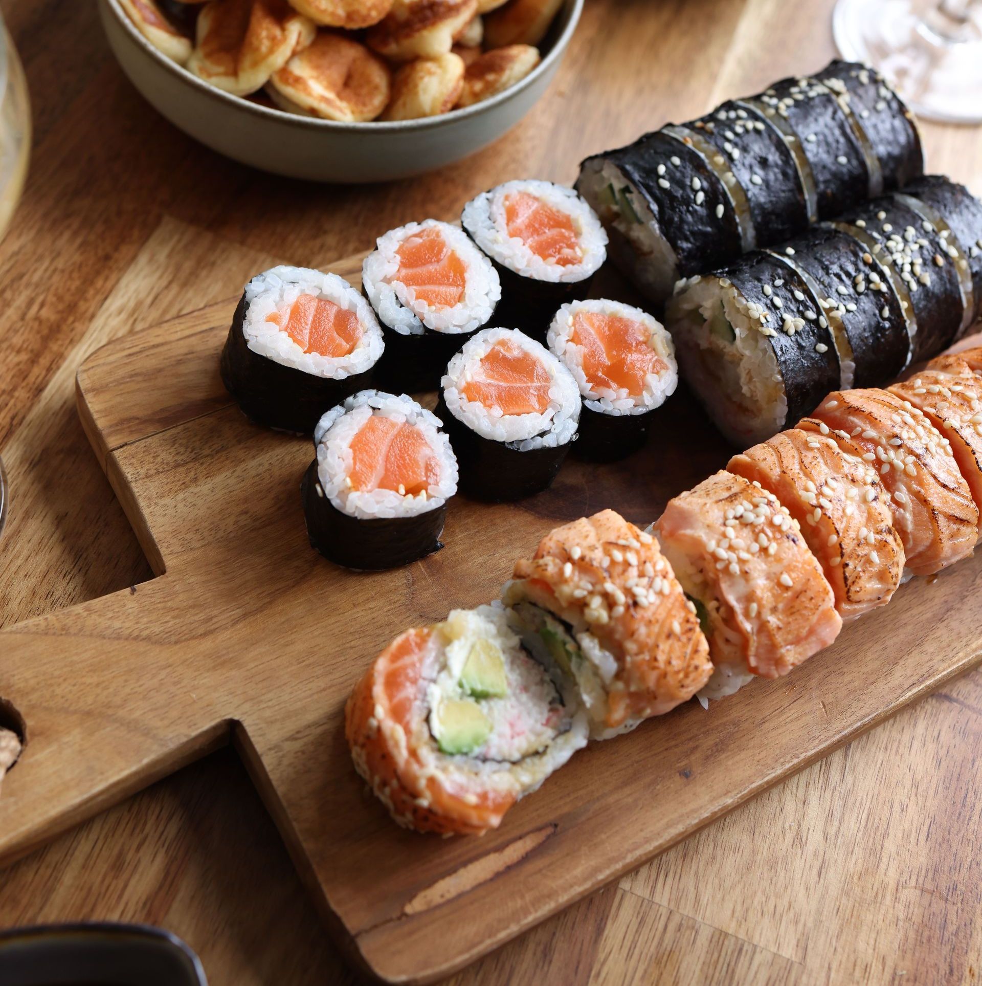 A selection of sushi rolls and snacks on a wooden platter, perfect for any meal.